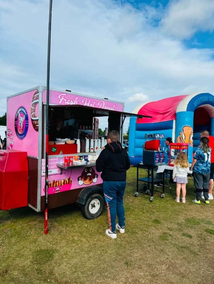Children and families ordering at the Angry Donut trailer at a family fun day with a bouncy castle